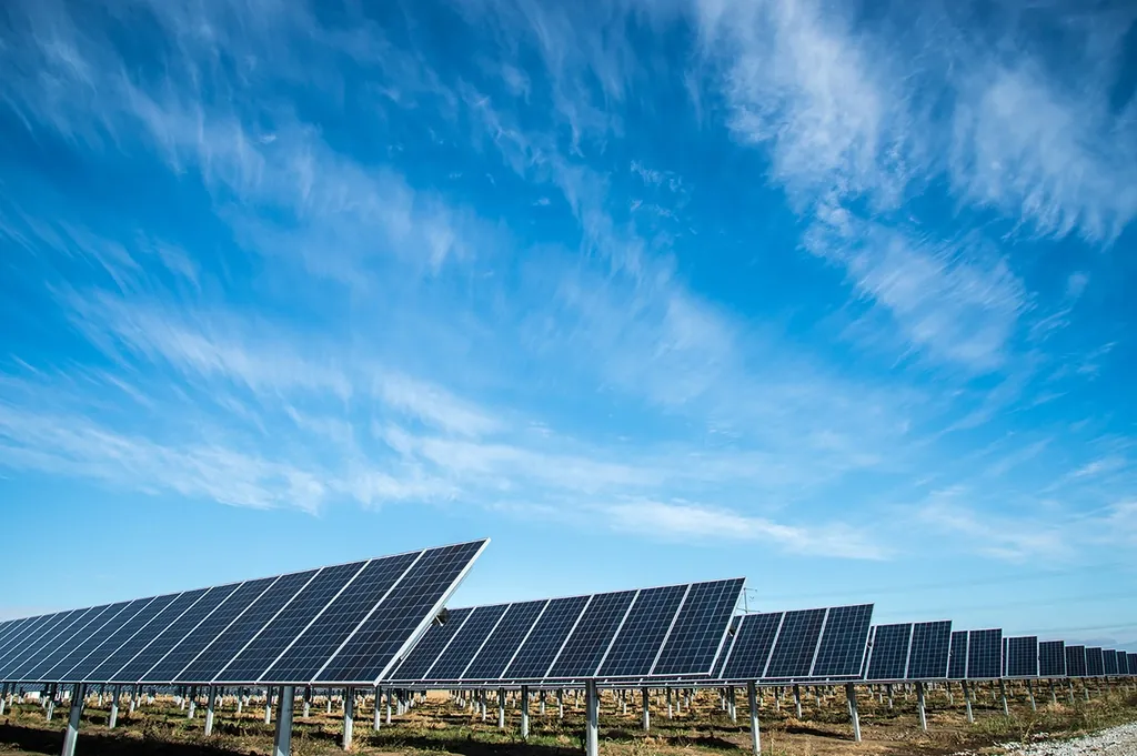 Rows of ground-mounted commercial solar panels under a blue sky