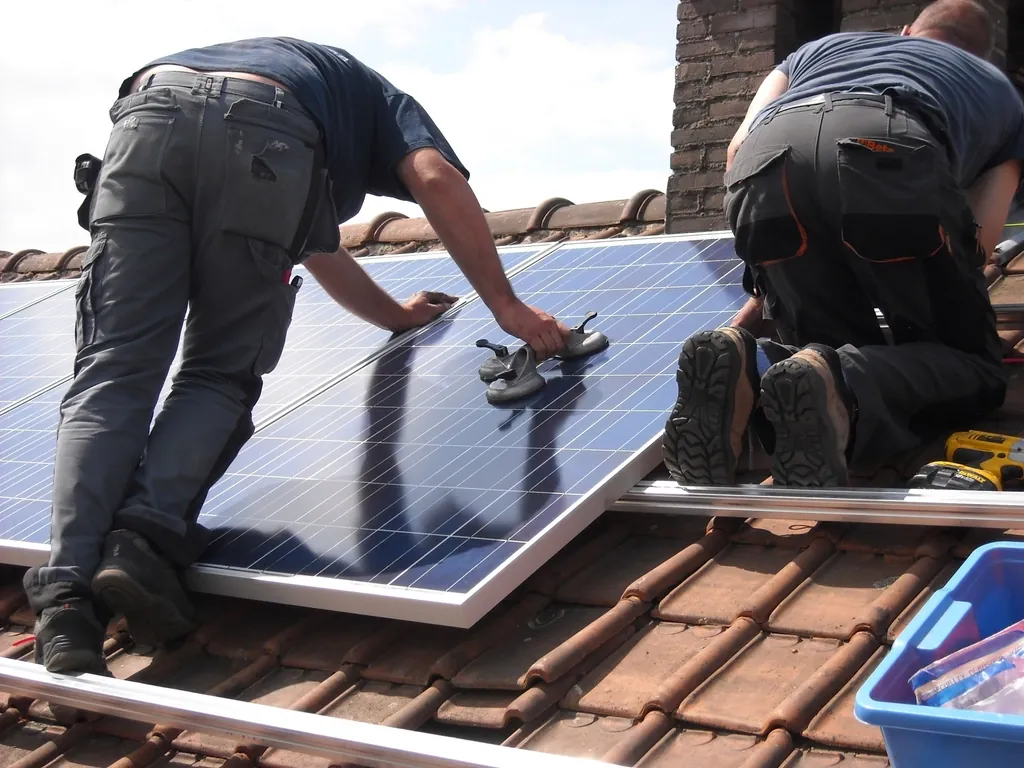 Two installers fitting solar panels onto mounting rails on a tile roof